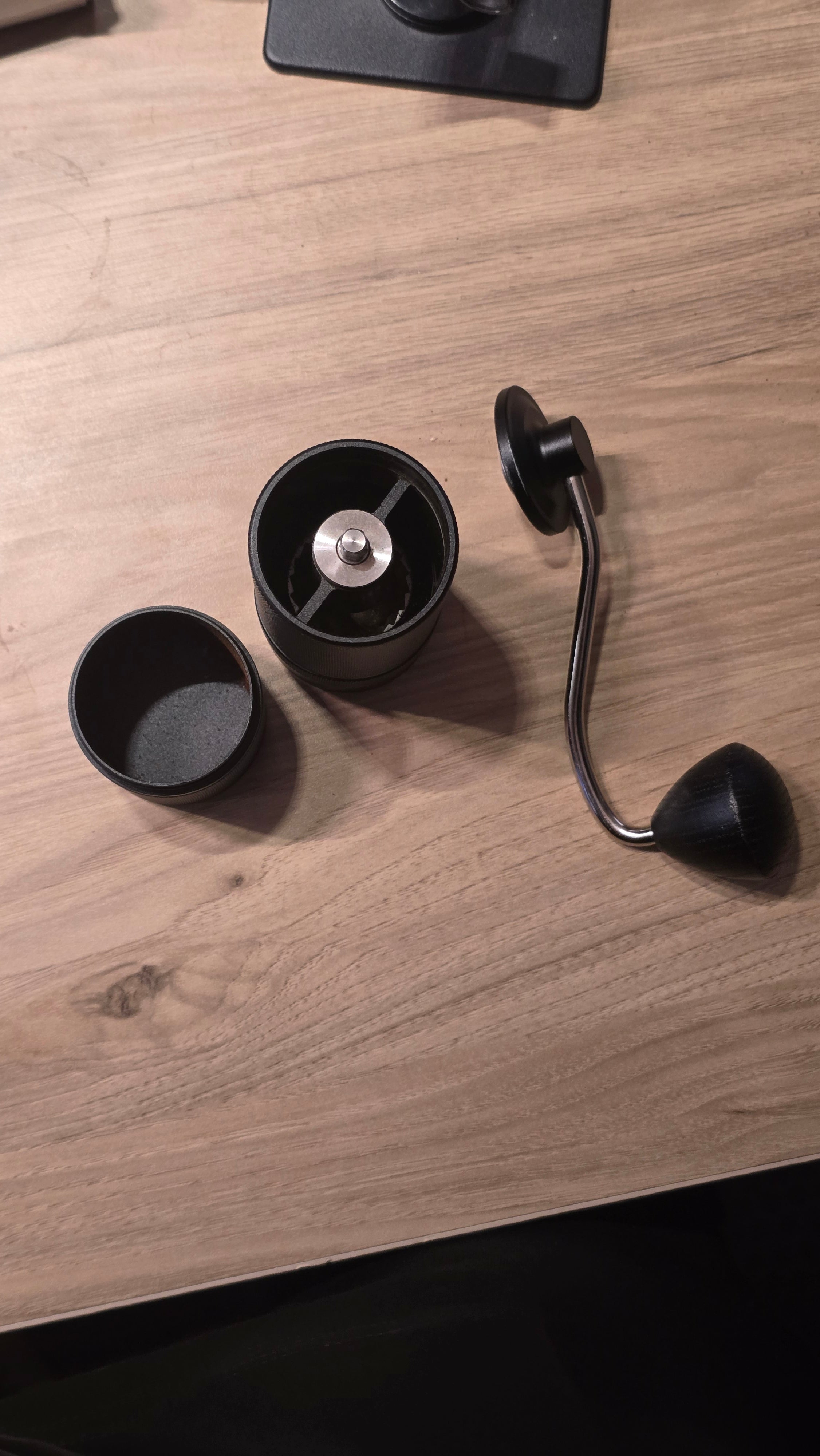 Molino de café manual negro con muelas cónicas visibles y manivela